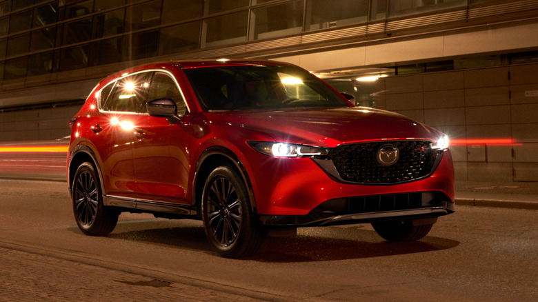 A red 2023 Mazda CX-5 on a roadway in front of a building.