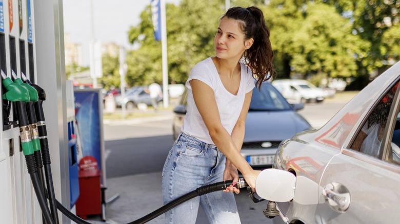 Young woman fills up her gas tank at gas station.