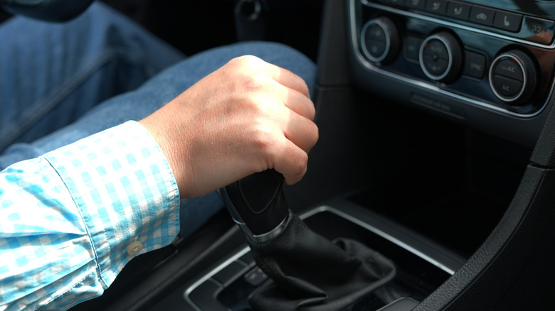 A close-up of a driver resting his hand on a car transmission lever.
