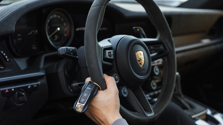 A person holding a Porsche steering wheel.