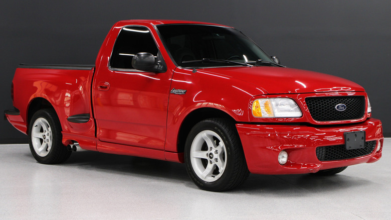 Front three-quarters shot of the bright red F-150 Lightning parked on a white shop floor in front of a black background