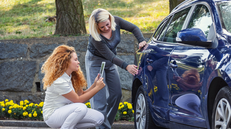 Two people looking at a dent in a blue car