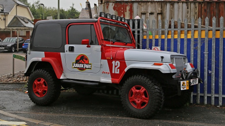 A Jurassic Park Jeep Wrangler parked near a fence.
