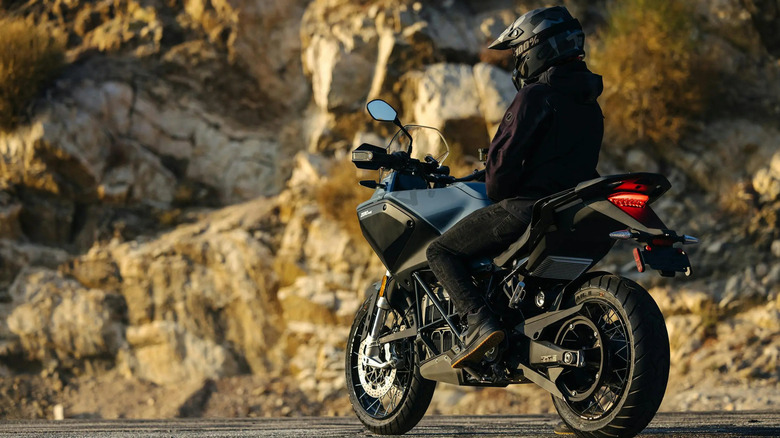 A rider sits atop an electric motorcycle outdoors near cliffs.