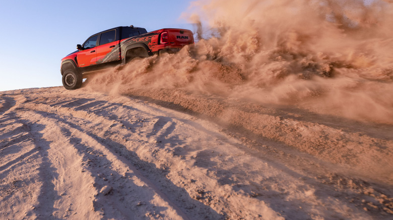 A red offroad performance pickup truck 2027 Ram 1500 TRX SRT blasts through desert sand.