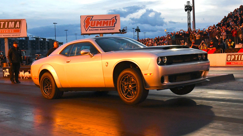 A silver Challenger's wheels leave the ground and is launches at a drag racing event.