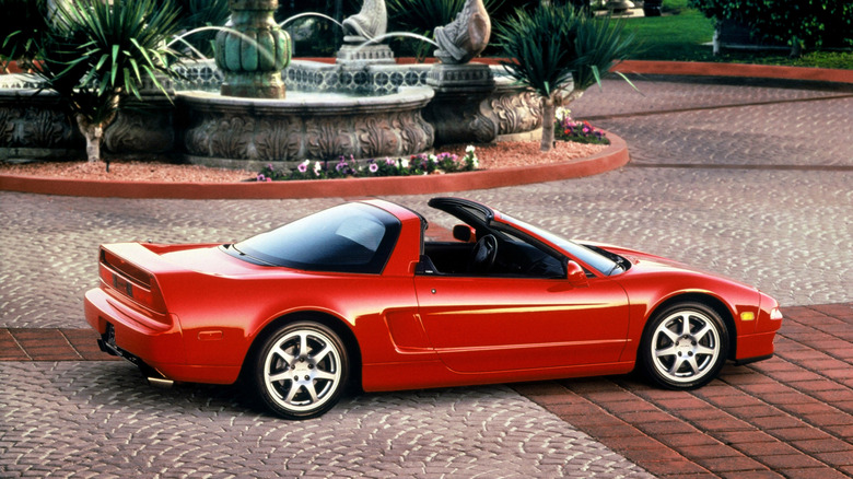 A red 1995 Acura NSX-T targa-top sports car parked on a stone courtyard near an ornamental fountain.
