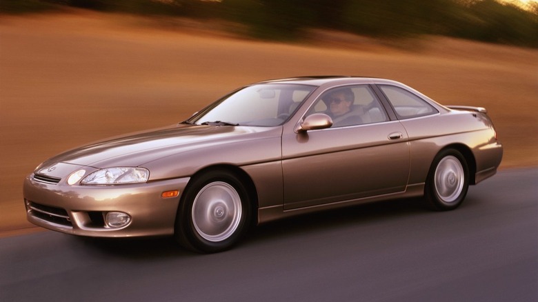 A gold Lexus SC 400 luxury coupe driving along a paved road.