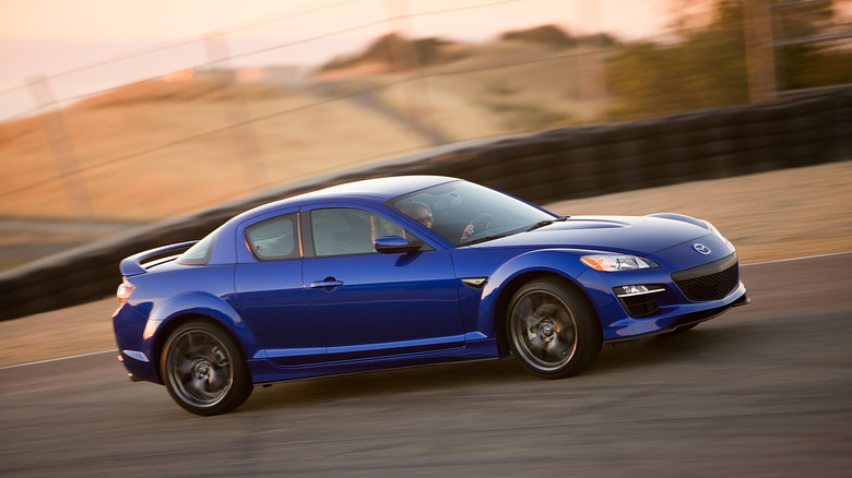 A blue Mazda RX-8 sports coupe driving around a paved race track.