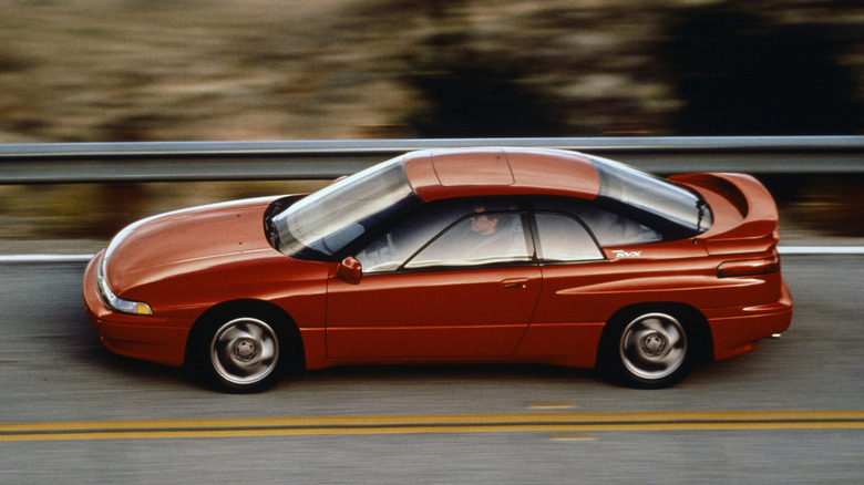 A red Subaru SVX sports coupe driving past a highway guardrail.