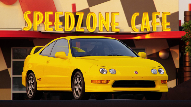 A yellow 2000 Acura Integra Type R DC2 parked in front of a Speedzone Cafe building with glowing neon lights.