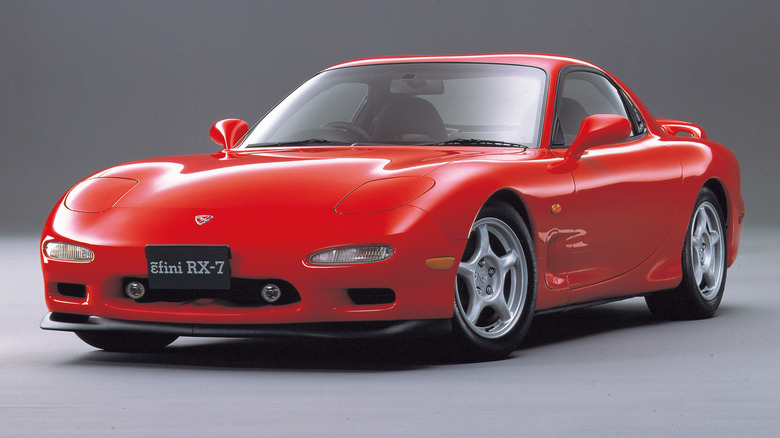 A bright red third-generation Mazda RX-7 FD sports car against a neutral gray background.