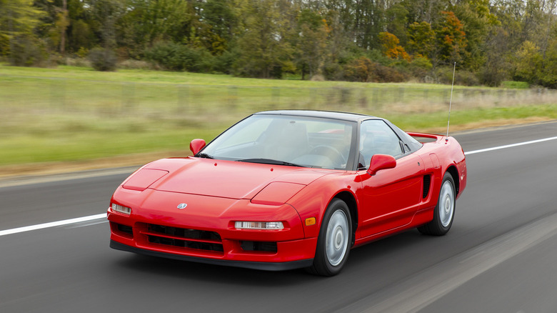 A red 1991 Acura NSX coupe driving along a scenic road.