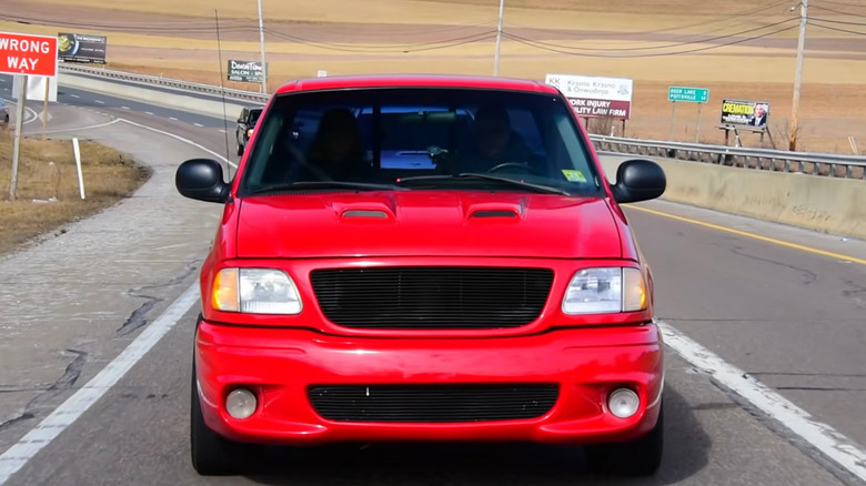 A red Ford F-150 SVT Lightning pickup truck driving down a road, front view.