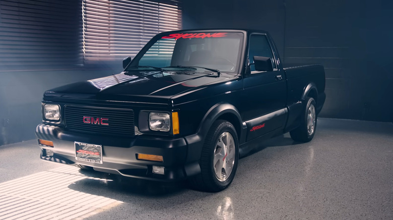 A black performance GMC Syclone pickup with red lettering sits in a garage under dramatic lighting.