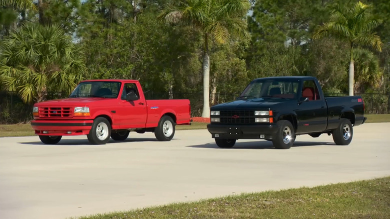 Red and black '90s muscle trucks vie for supremacy side-by-side on white pavement.