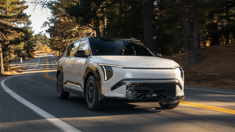 Front 3/4 of 2027 Kia EV3 driving on road through a forest