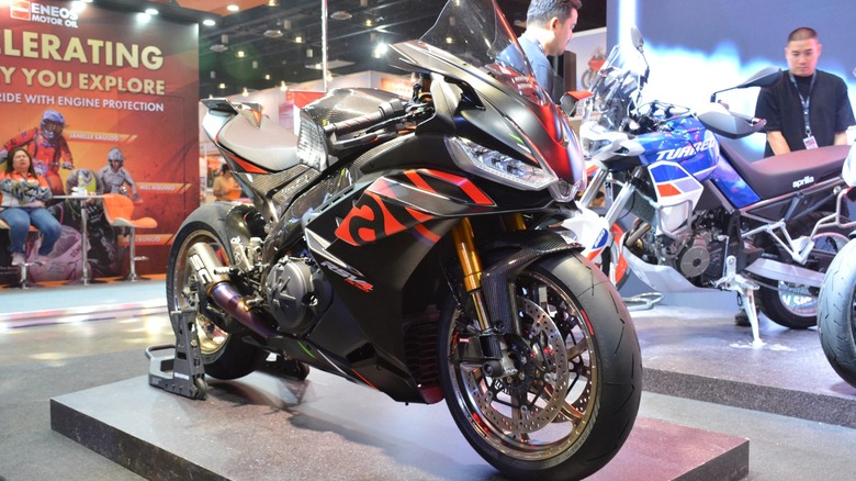 A black-and-red Aprilia RSV4 Factory 1100 parked on an exhibition stand at a motor show.