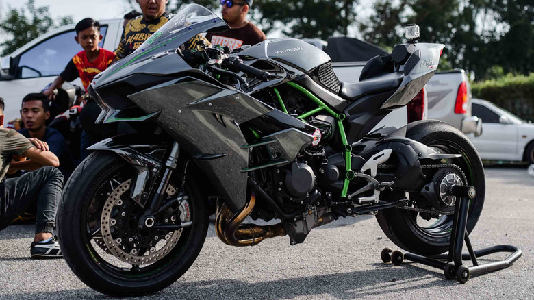 A Kawasaki H2R in a parking lot next to a group of people.