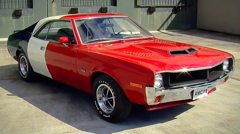 A 1970 American Motors Javelin in red, white, and blue racing livery parked in a concrete lot.