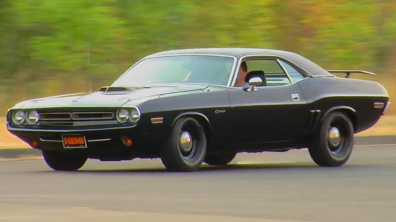 A black 1970 Dodge Challenger R/T driving on a track with a shaker hood