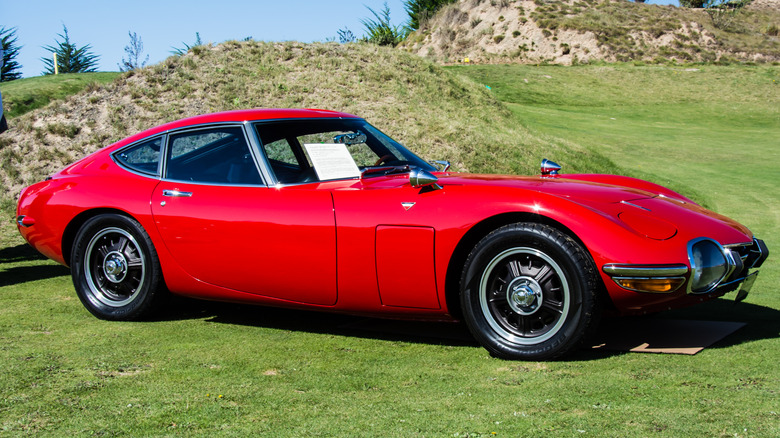 A red Toyota 2000GT sits on concourse grass.