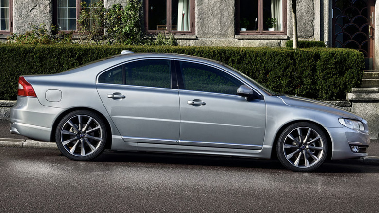 A silver Volvo S80 parks on a sloped street.