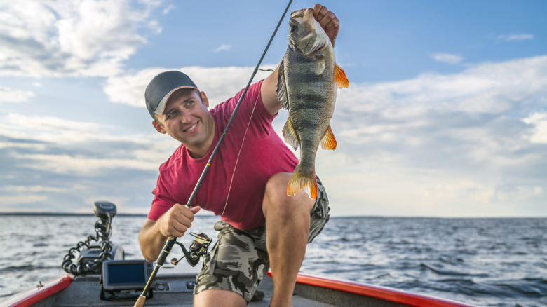 Man in small boat proudly holding up caught fish