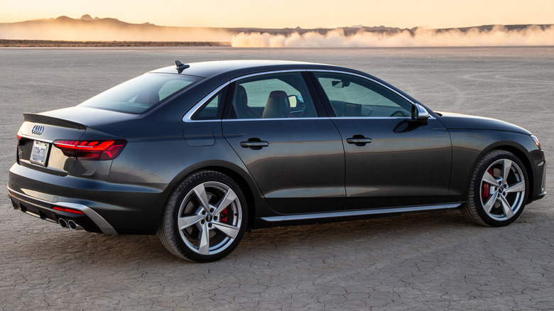 A gray Audi S4 on an unpaved surface with hills in the background.