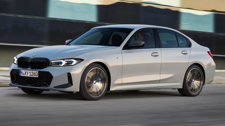 A gray BMW 3 Series being driven in front of a building.