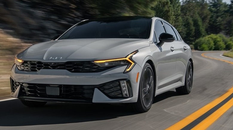 A gray 2026 Kia K5 in motion on a roadway.
