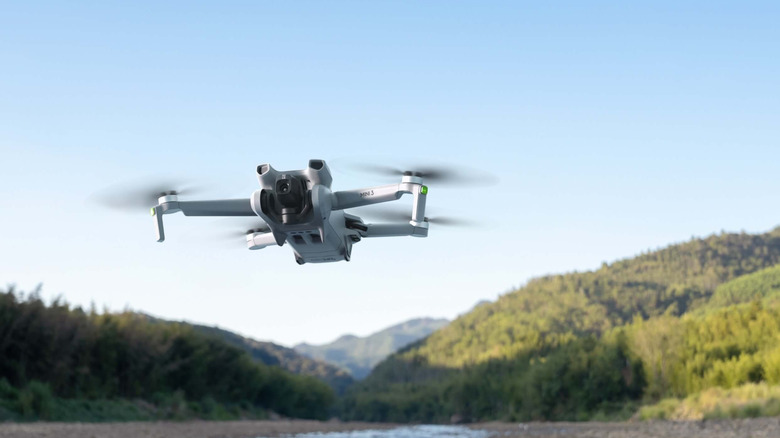 A DJI Mini 3 flying over water with mountains and a blue sky in the background