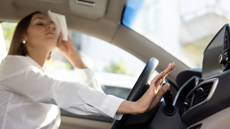 Woman wiping sweat from her face inside a hot car.