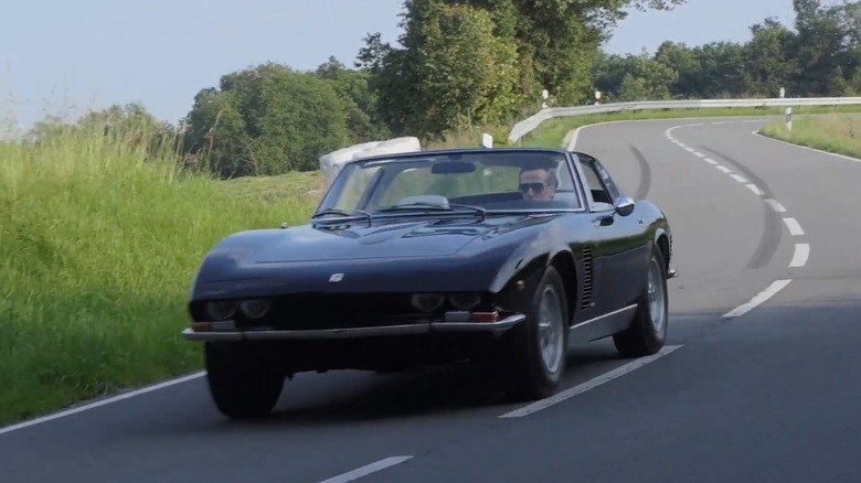 A person driving a black 1971 Targa-top Iso Grifo on a winding road
