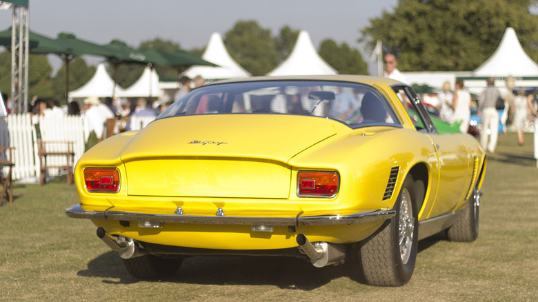 A rear shot of a yellow 1967 Iso Grifo parked on a short lawn at a fancy car event