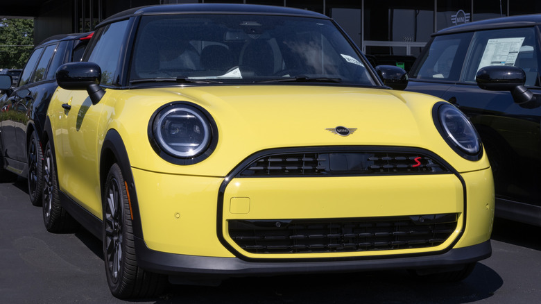 A bright-yellow Mini Cooper S parked outside a Mini dealership.