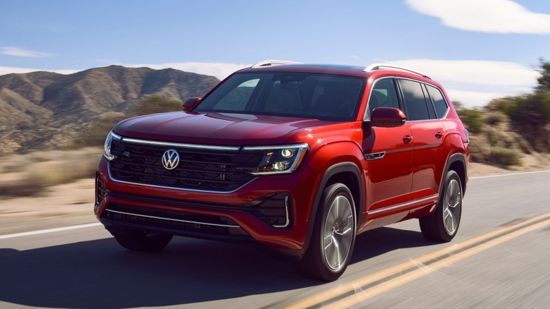 A red Volkswagen Atlas being driven on a two-lane road in front of hills.