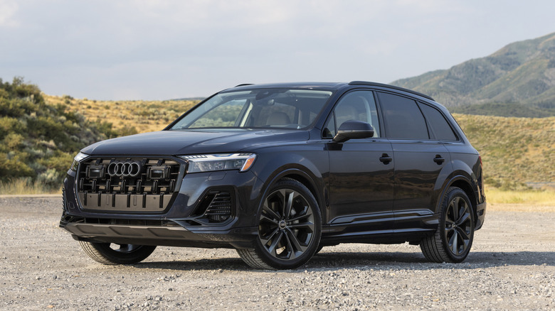 A dark blue Audi Q7 on an unpaved surface in front of hills.