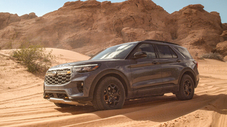A gray  being driven on a sandy trail amid shrubs and hills.