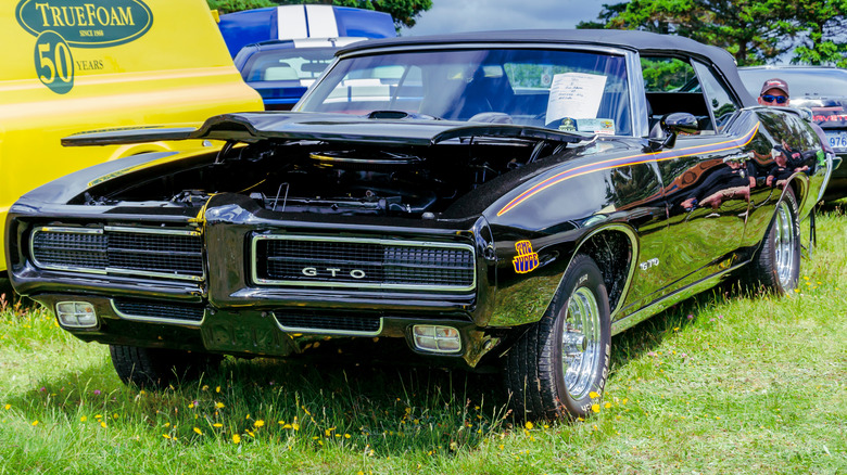 A black-colored, rare 1969 Pontiac GTO The Judge convertible parked on the grass at a car show.