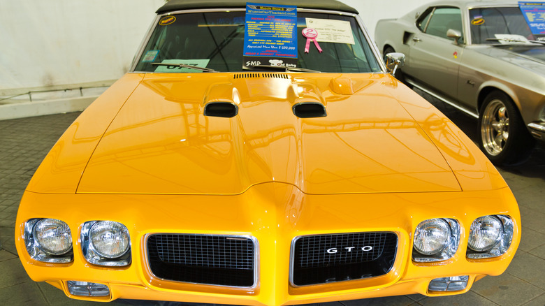 A vibrant yellow 1970s Pontiac GTO Judge convertible on display at a vintage car show.