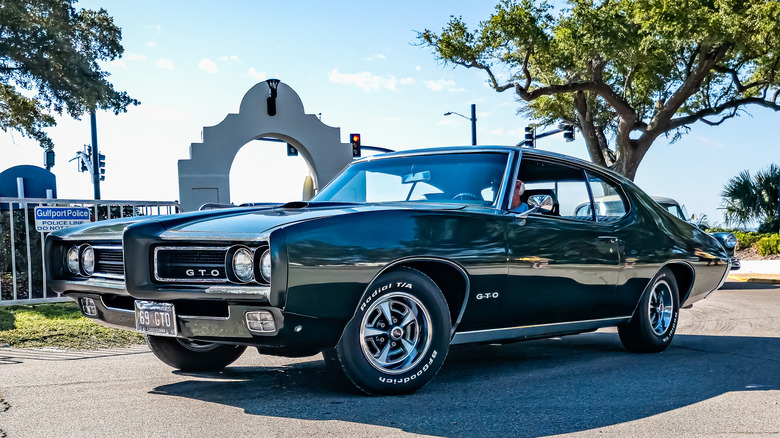 A dark-colored 1965 Pontiac GTO parked under a tree.