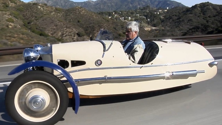 Jay Leno behind the wheel of a cream and dark blue 1932 Morgan Three-Wheeler.
