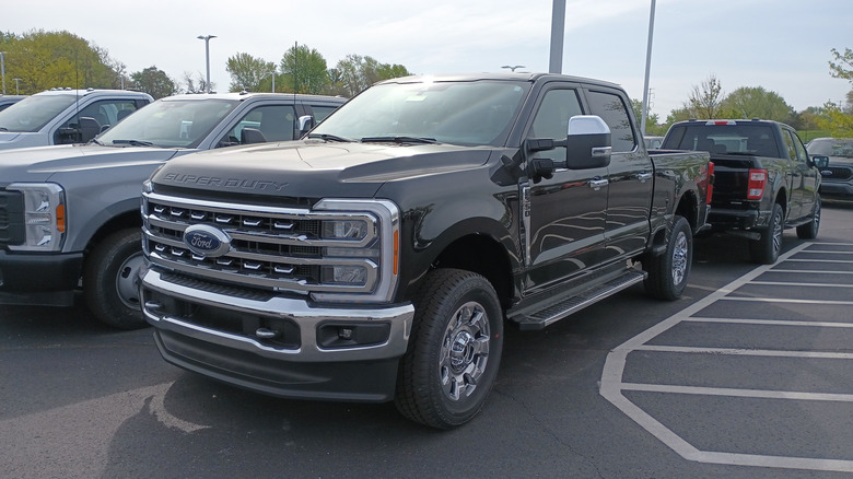 A front 3/4 view of a 2023 black Ford F-350 Super Duty Lariat SuperCrew parked in a lot with other cars in the background