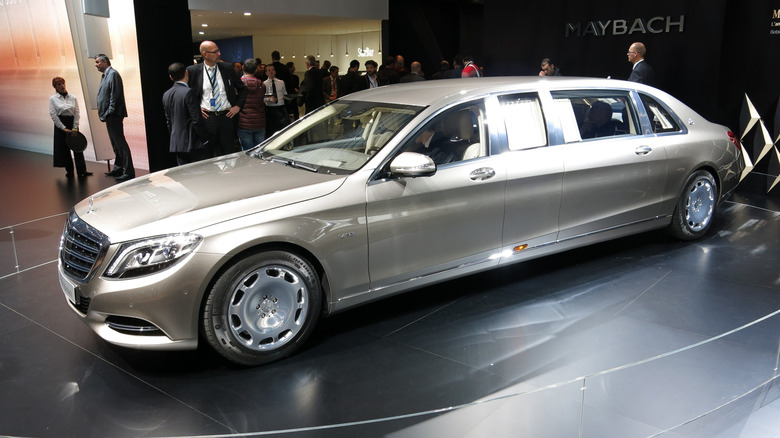 A silver-gold Mercedes-Maybach S600 Pullman on display with a group of people gathered behind