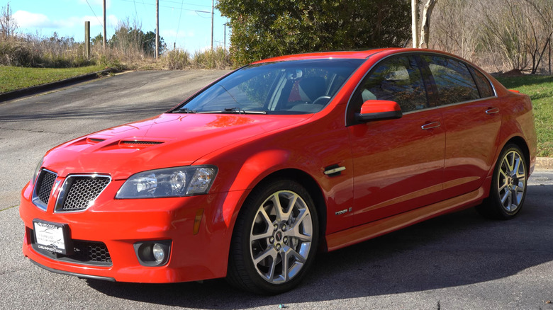 A bright red Pontiac G8 GXP performance sedan with hood scoops and alloy wheels parked in a lot.
