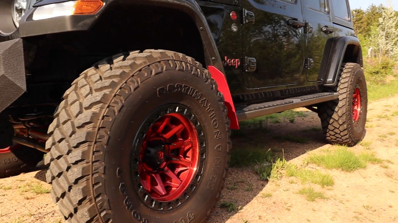A black Jeep Wrangler on a dirt path featuring a Firestone Destination M/T2 tire mounted on a red accent wheel.