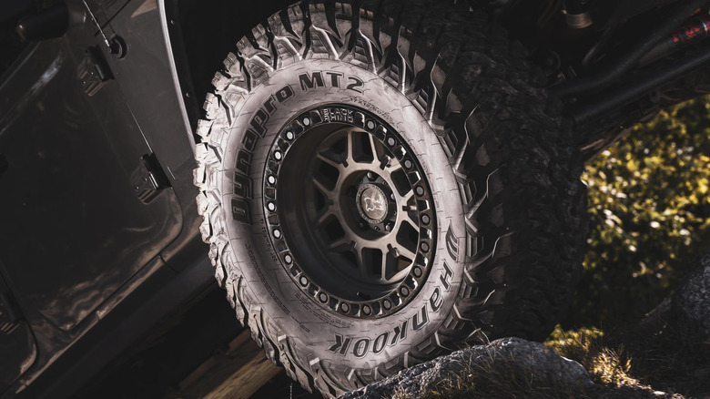 A Hankook Dynapro MT2 tire mounted on a black beadlock-style wheel pressed against a rock.