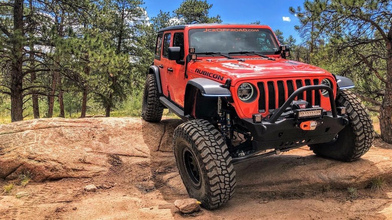 An orange Jeep Wrangler Rubicon articulated over a rock outcropping on Mickey Thompson Baja Boss M/T tires.