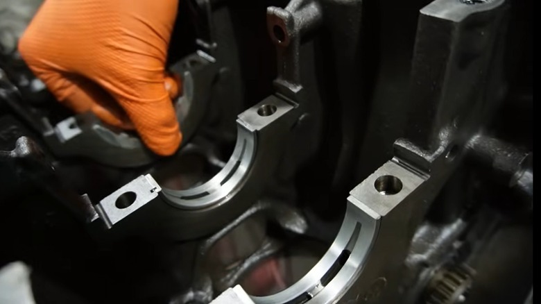 Mechanic's hand in an orange glove handles a thrust washer in a disassembled crankshaft